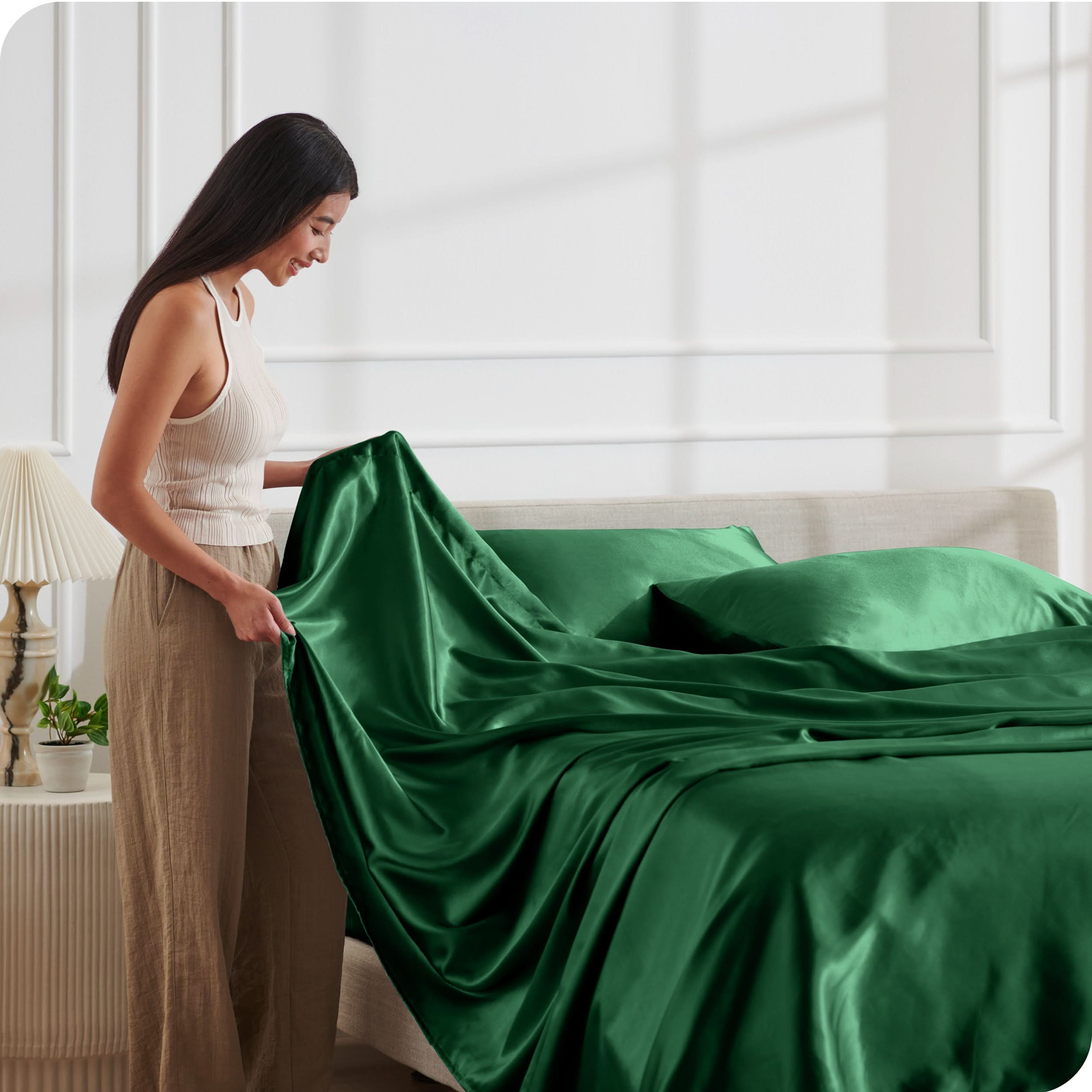 A woman is putting satin sheets on a bed