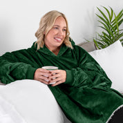 A woman sitting on a couch holding a mug wearing a sherpa blanket.