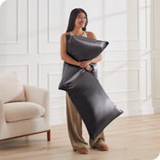 A woman standing while holding pillows with silk pillowcases on them