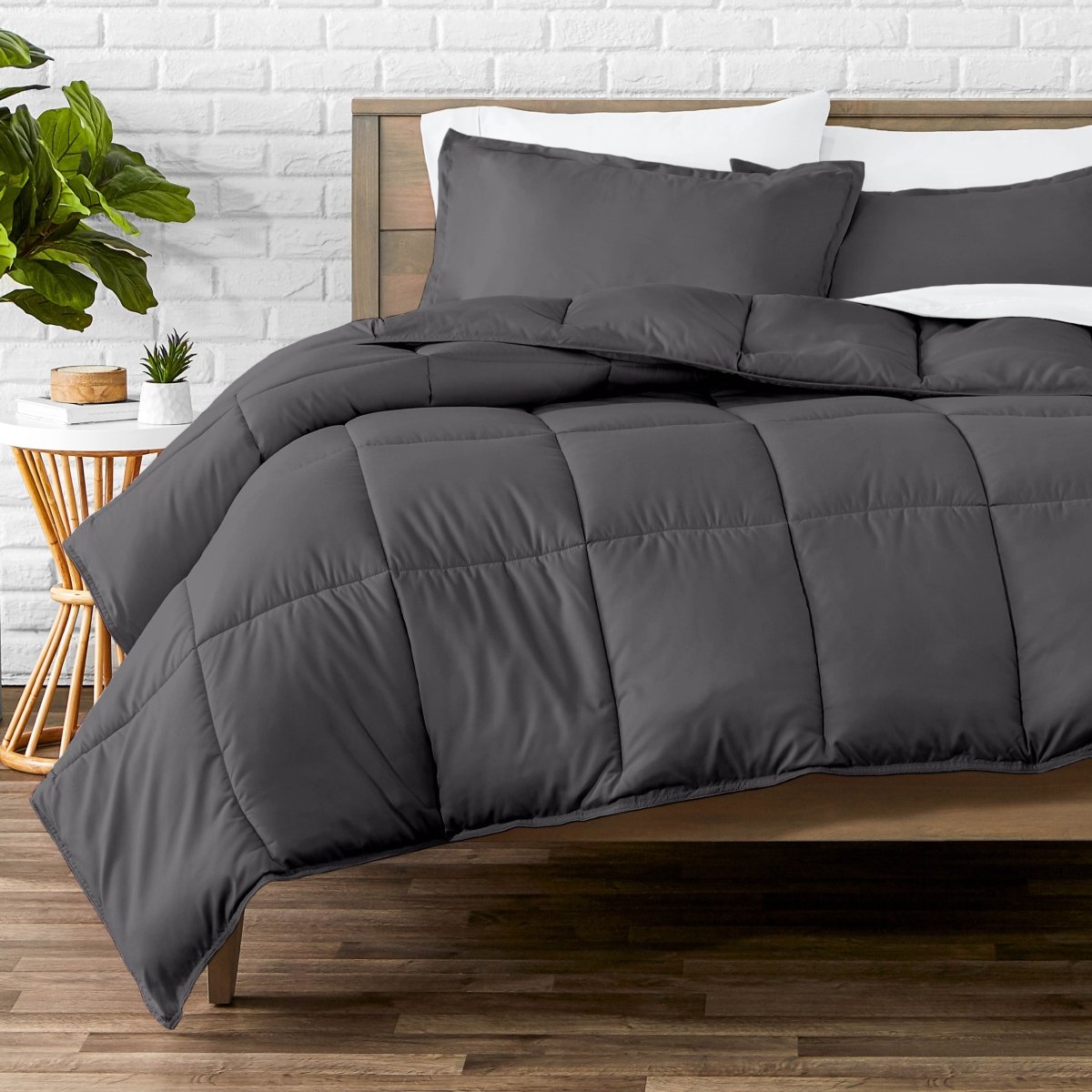 Comforter set on a bed with a white brick wall and plant in the background