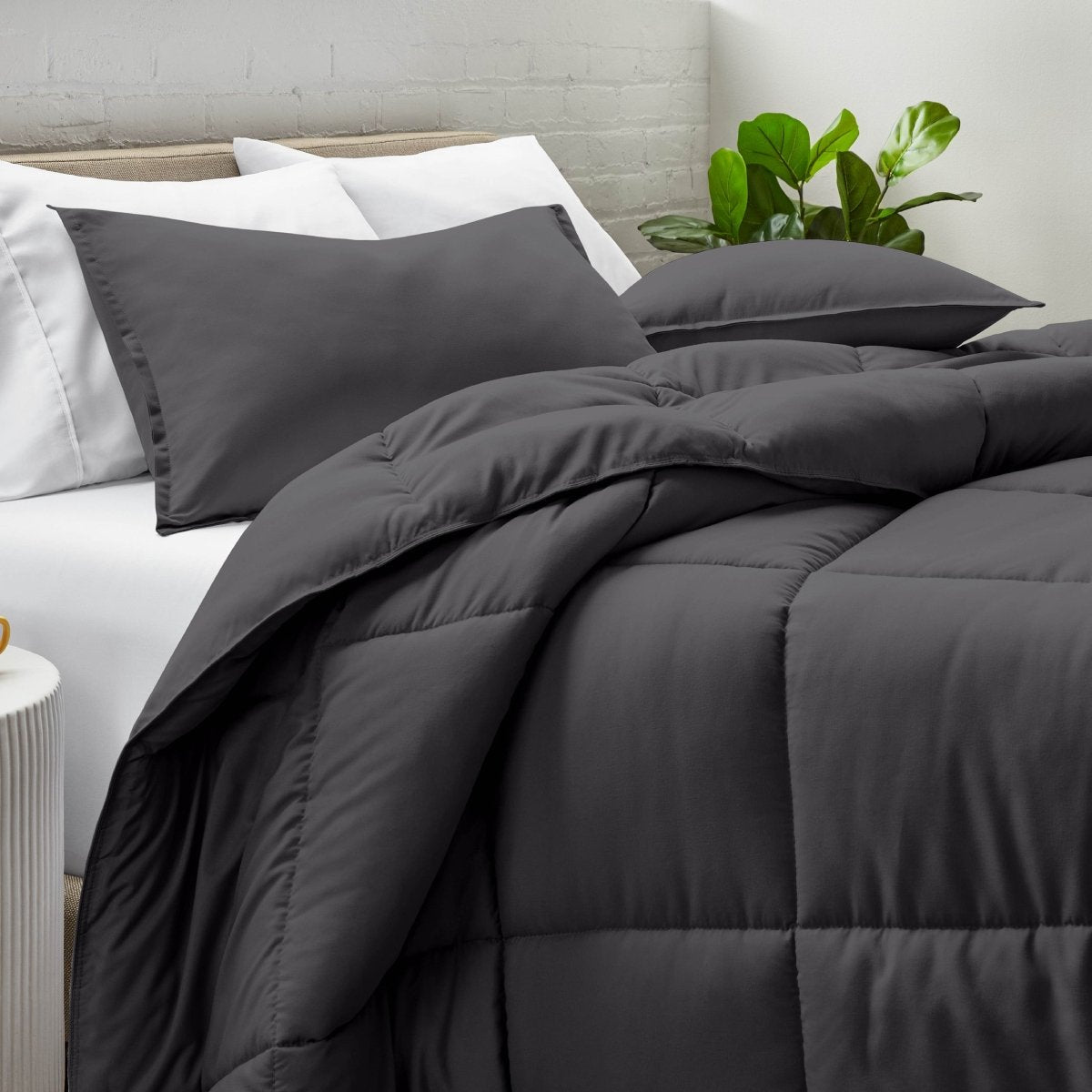 Comforter and pillow shams on a bed with a white brick wall and plant in the background