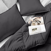 Comforter and pillows on a bed with a magazine and glasses.