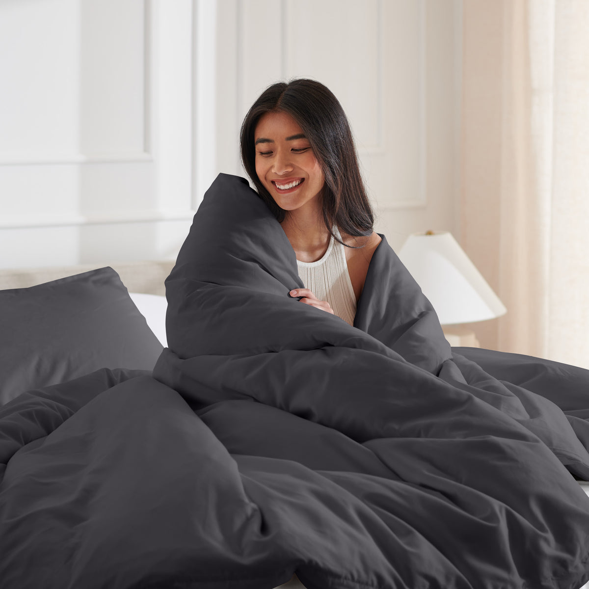 Woman smiling under duvet cover set in a bedroom setting