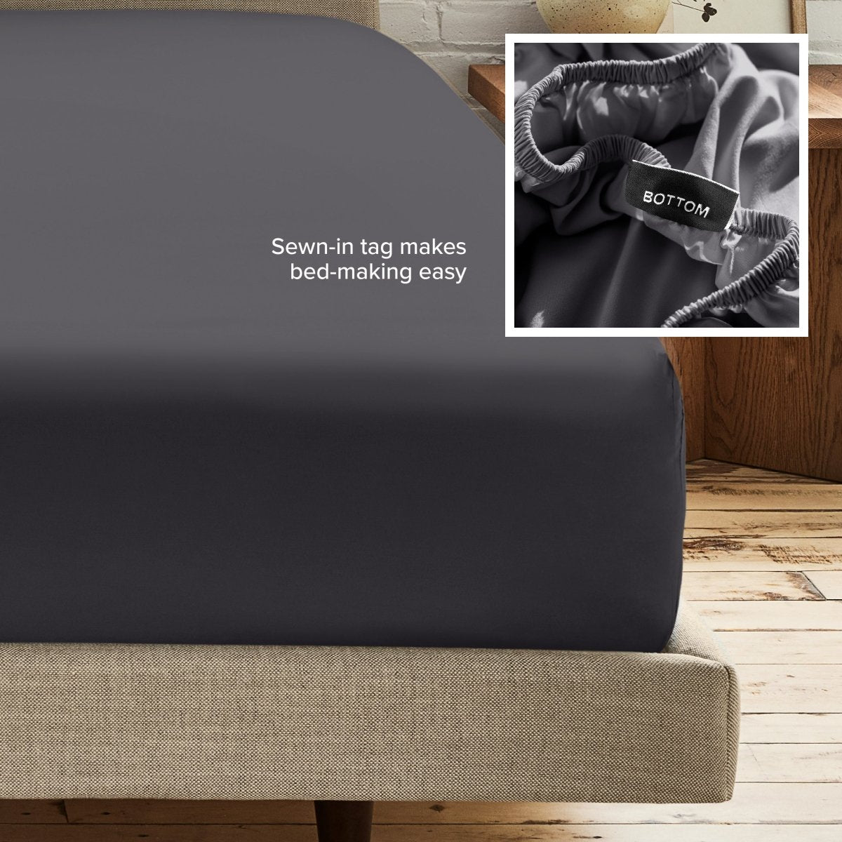 A fitted bed sheet on a bed frame with a small inset close-up of the elastic and a sewn-in tag labeled BOTTOM. White text on the sheet reads, 'Sewn-in tag makes bed-making easy.
