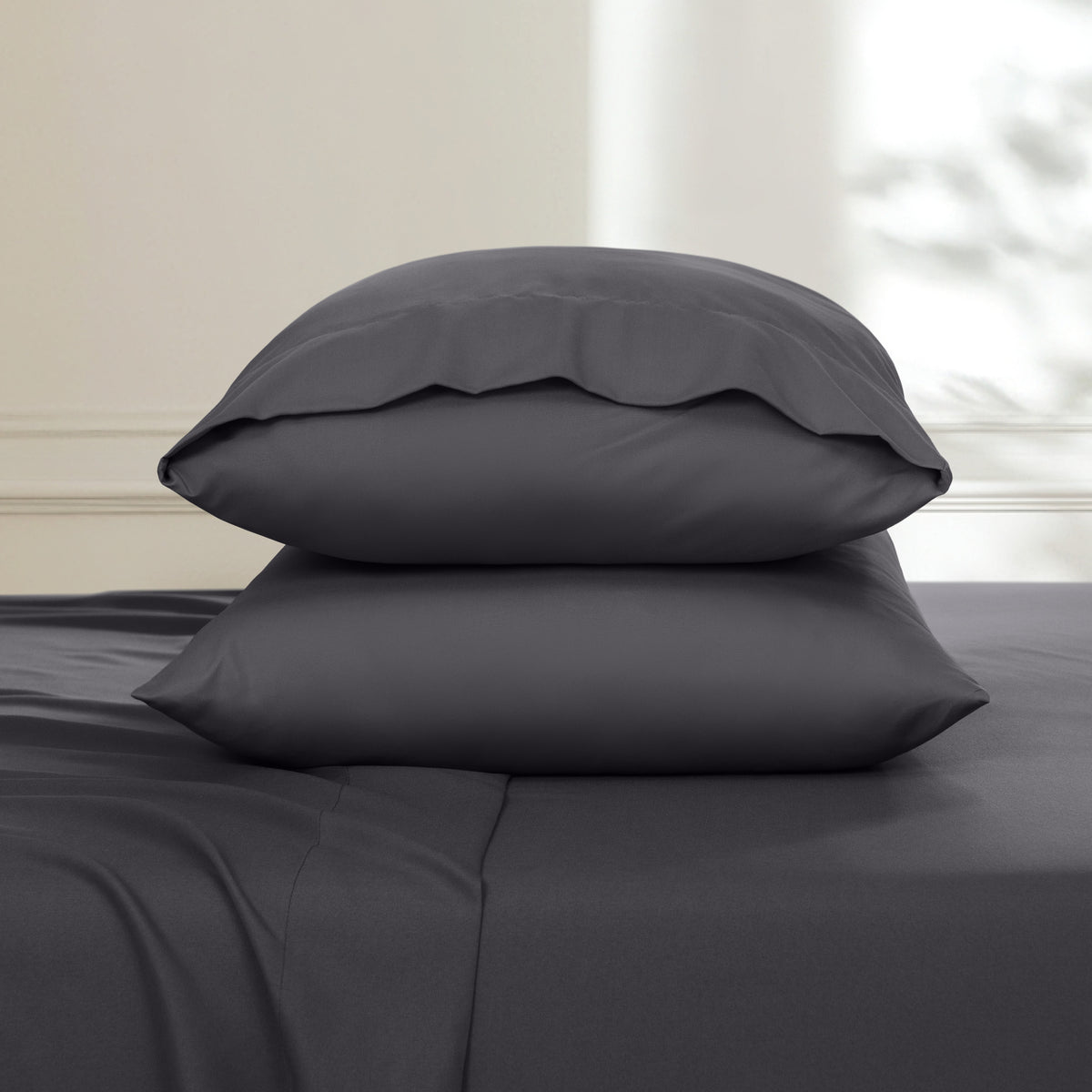 Two pillows stacked on a bed with a neutral background