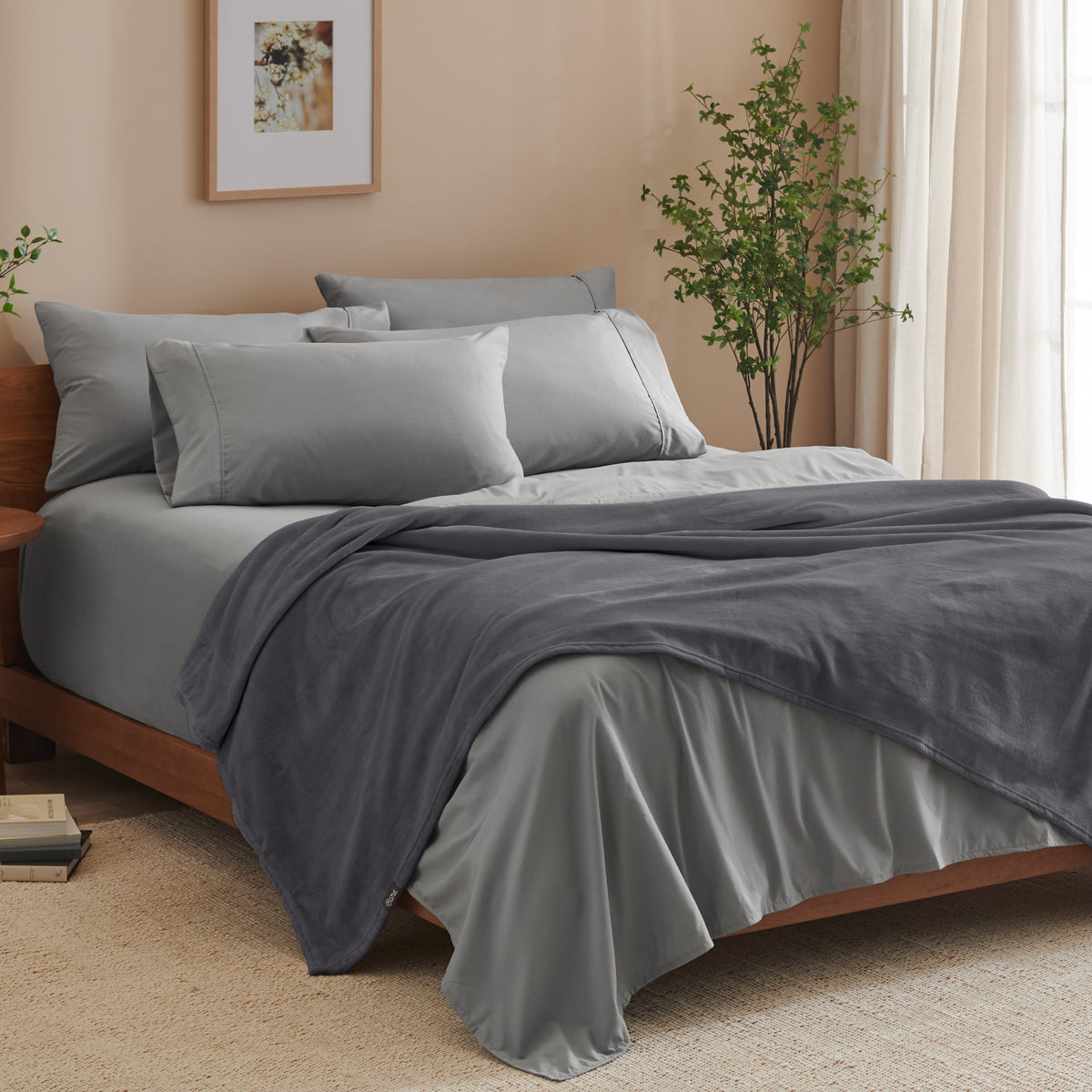A bed made with grey sheets and a microplush blanket