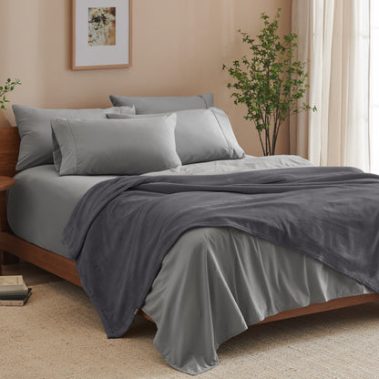 A bed made with grey sheets and a microplush blanket