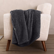 Faux shearling blanket draped over a beige armchair with a wooden base.