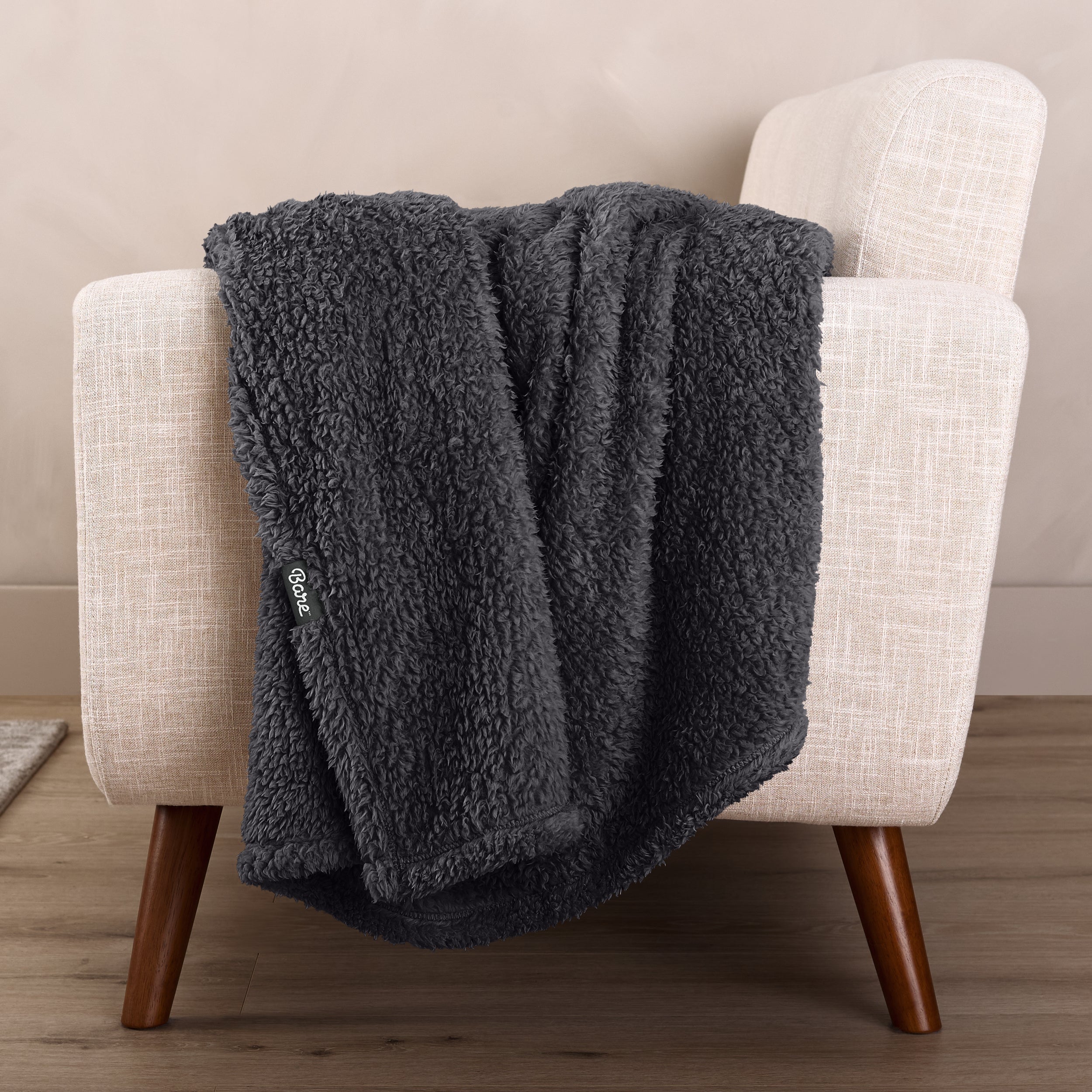 Faux shearling blanket draped over a beige armchair with a wooden base.