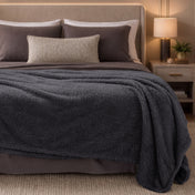 Bed with dark gray blanket and pillows in a bedroom setting