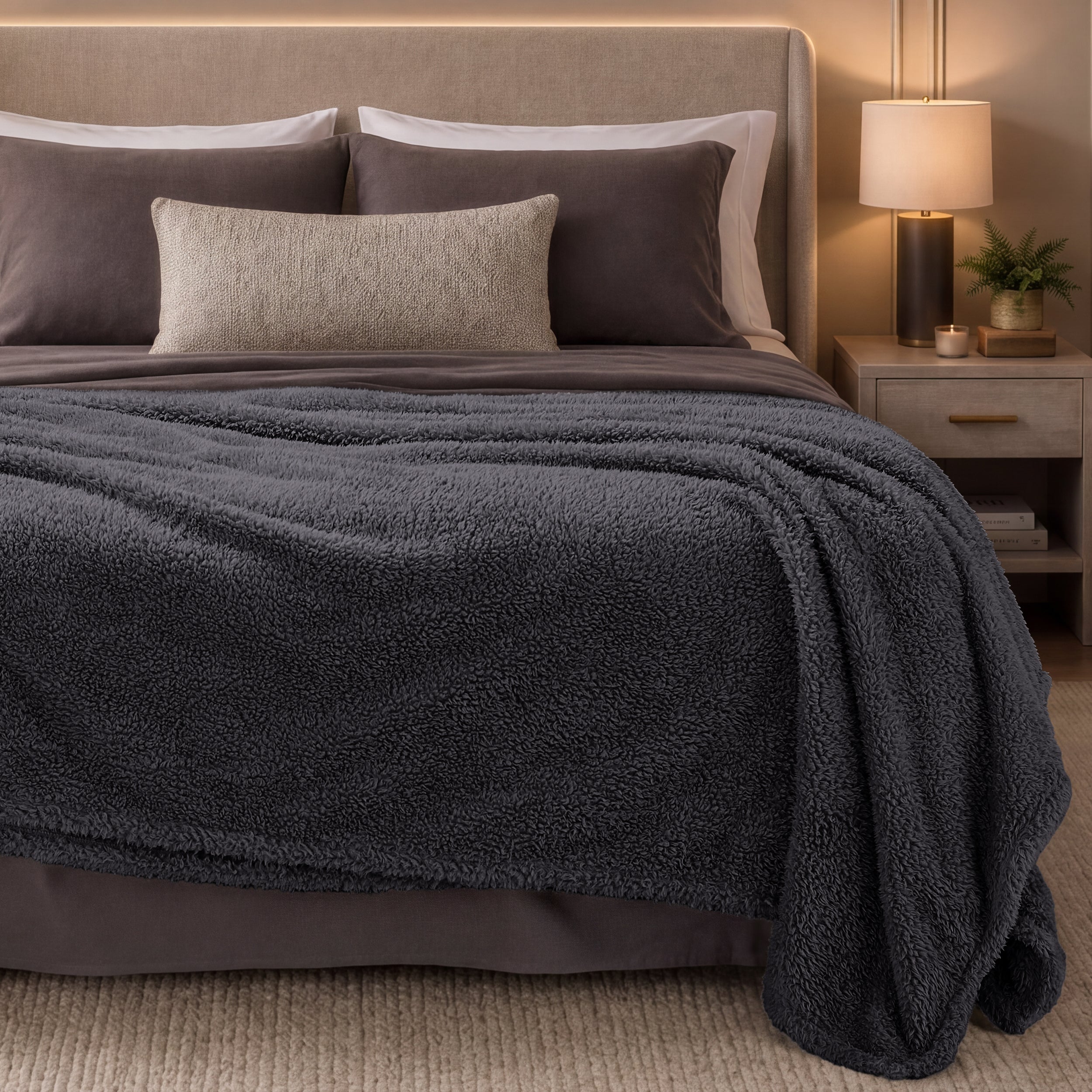 Bed with dark gray blanket and pillows in a bedroom setting