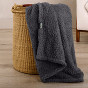 Fluffy blanket draped over a woven basket on a wooden floor.
