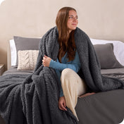 A woman sitting on a bed wrapped in a sherpa blanket