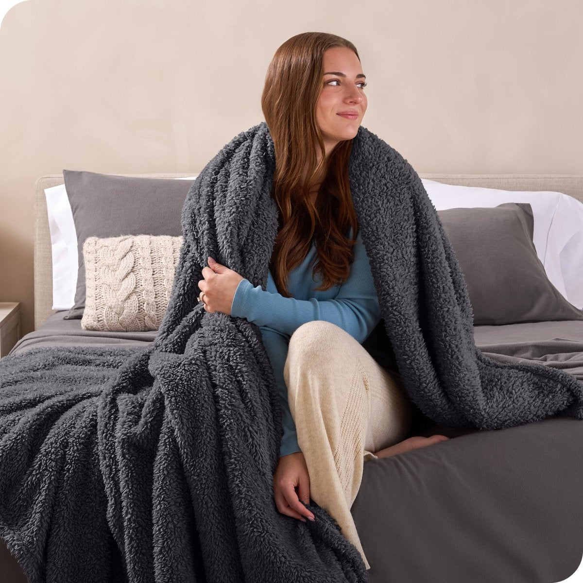 A woman sitting on a bed wrapped in a sherpa blanket