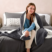 A woman sitting on a bed with a Sherpa blanket around her