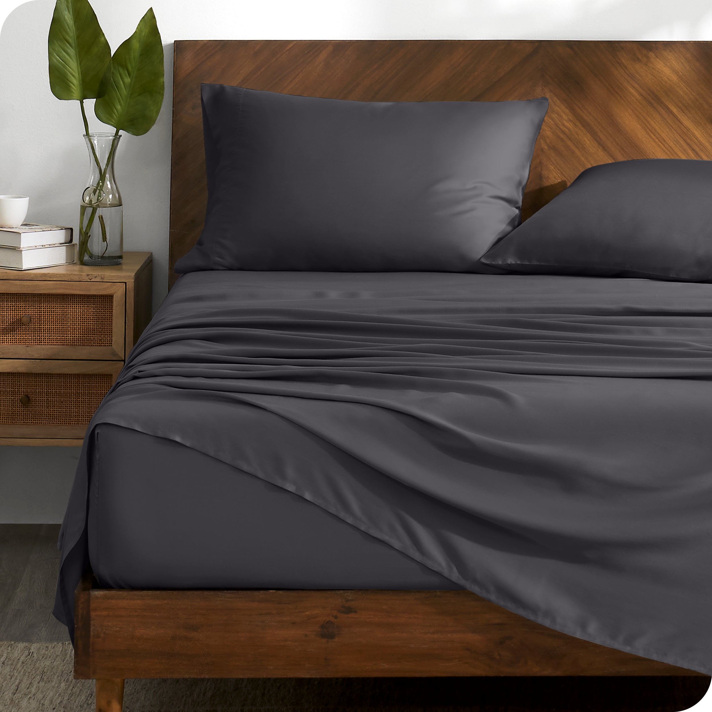TENCEL™ sheet set on a bed with the flat sheet loosely draped over the top. The mattress is on a wooden bed frame. 