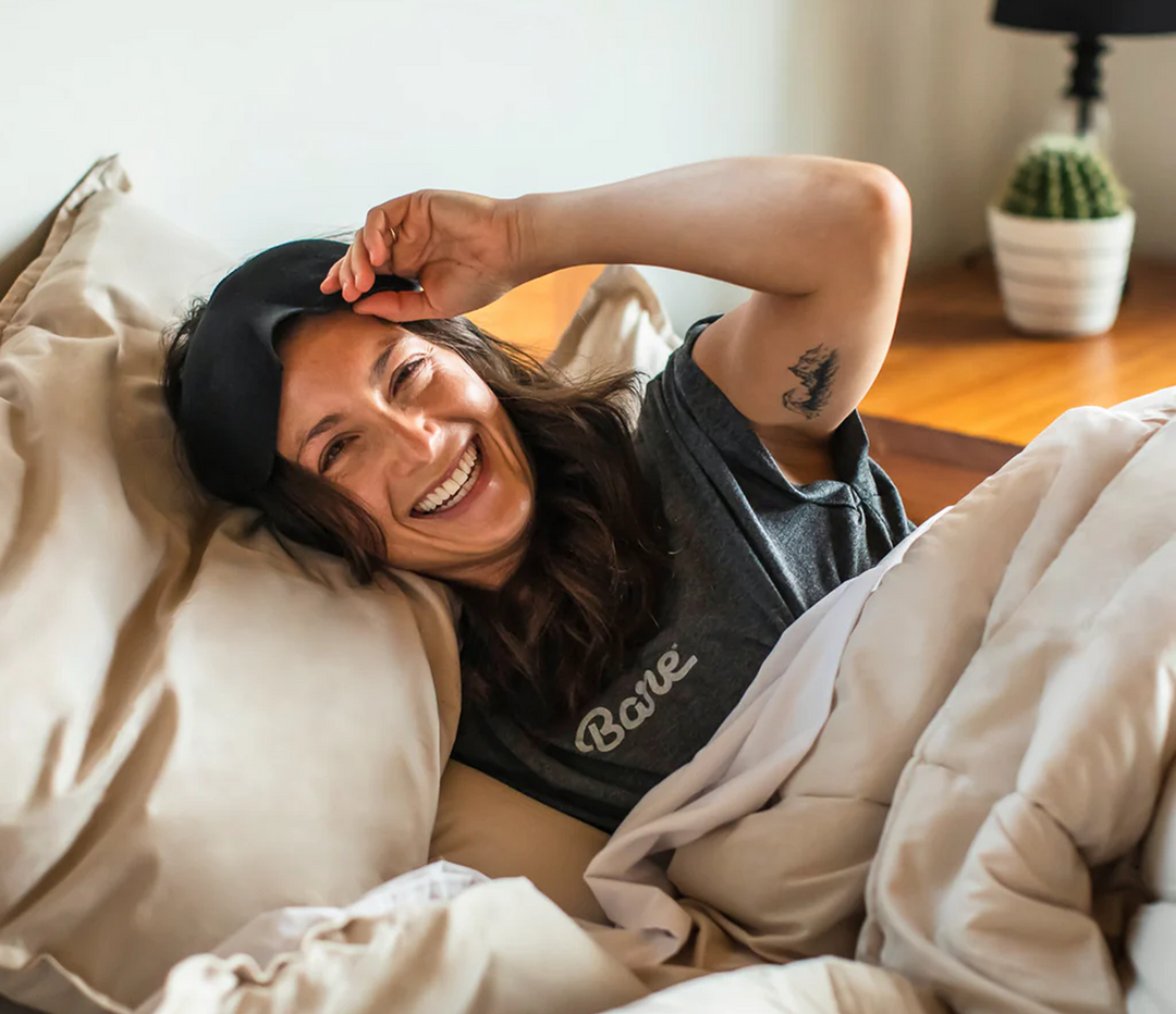 Woman smiling while lying in bed with tan bedding