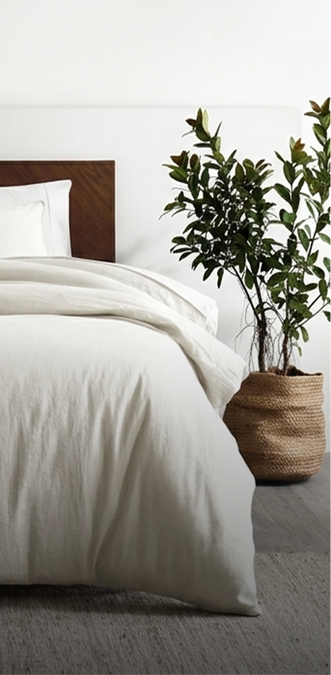 Bedroom with white bedding, wooden headboard, and a plant in a woven basket.