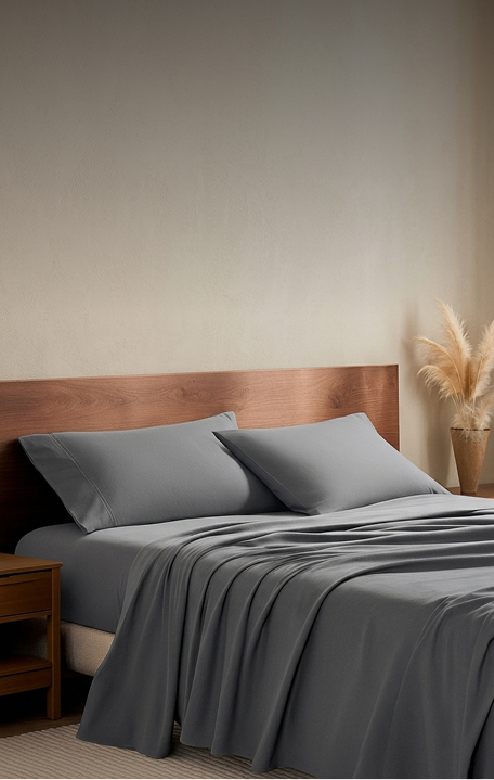 Gray bedding set on a bed with a wooden headboard in a bedroom setting.