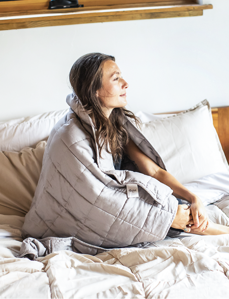 Woman sitting on a bed wrapped in a gray blanket review