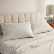Percale bed sheets and pillowcases on a neatly made bed with a beige headboard.