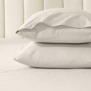 Two pillows stacked on a bed with percale pillowcases on them