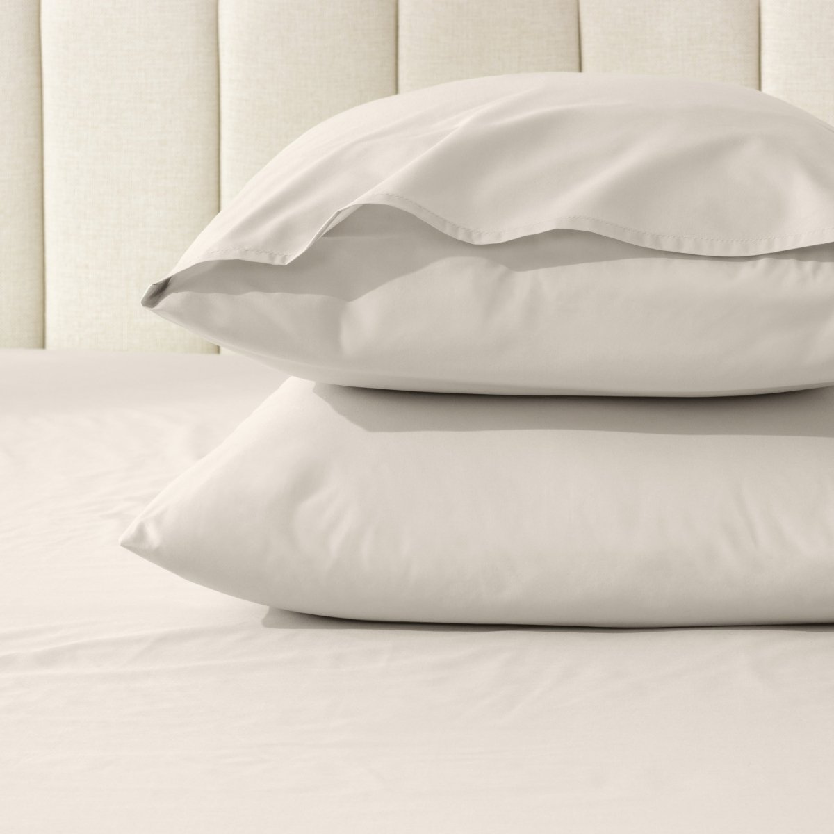 Two pillows stacked on a bed with percale pillowcases on them