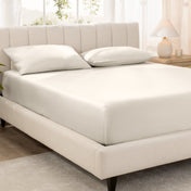 Bed with fitted sheet and pillowcases in a bright room.