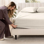Woman adjusting a fitted sheet on a bed in a bedroom setting
