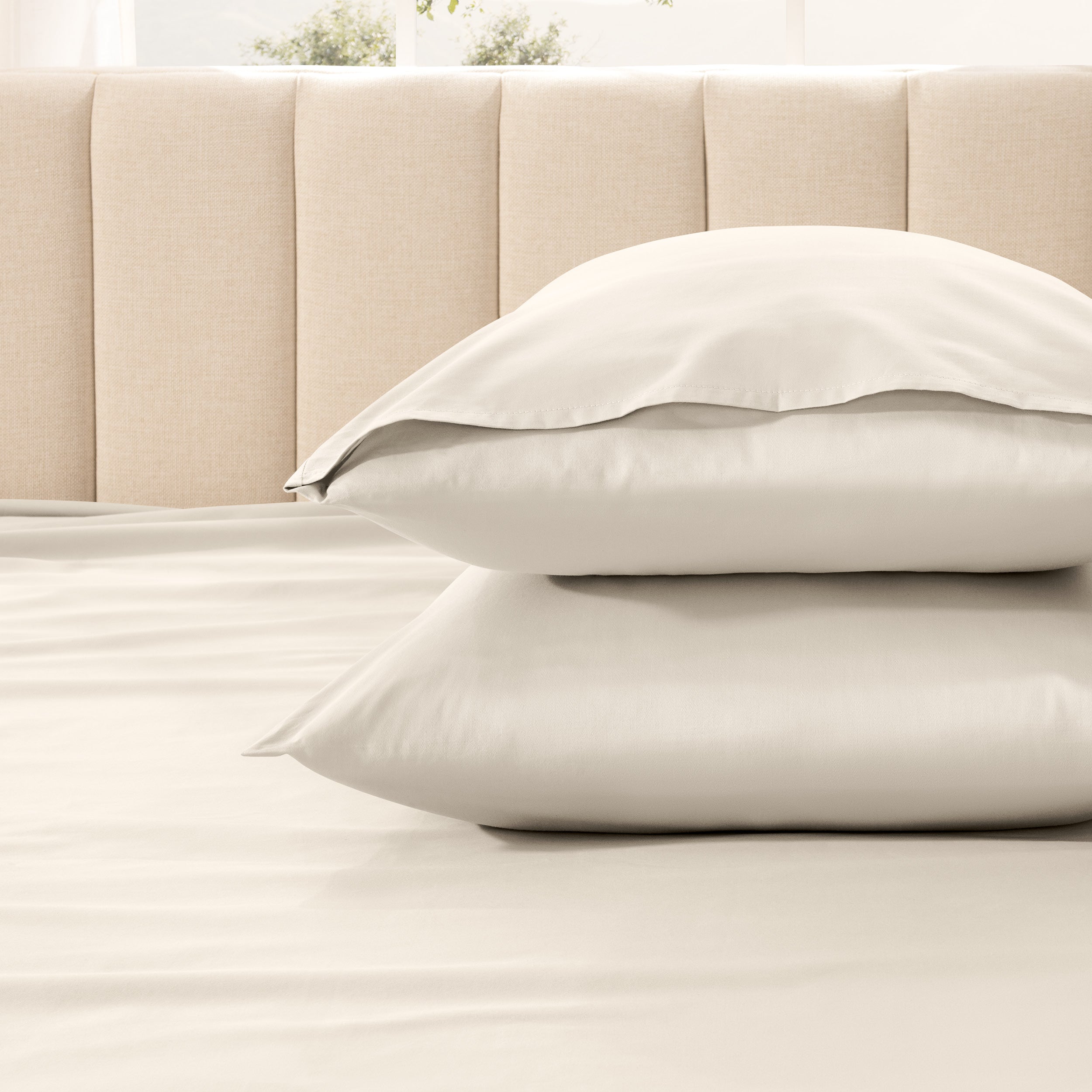 Two pillows stacked on a bed with a beige headboard.