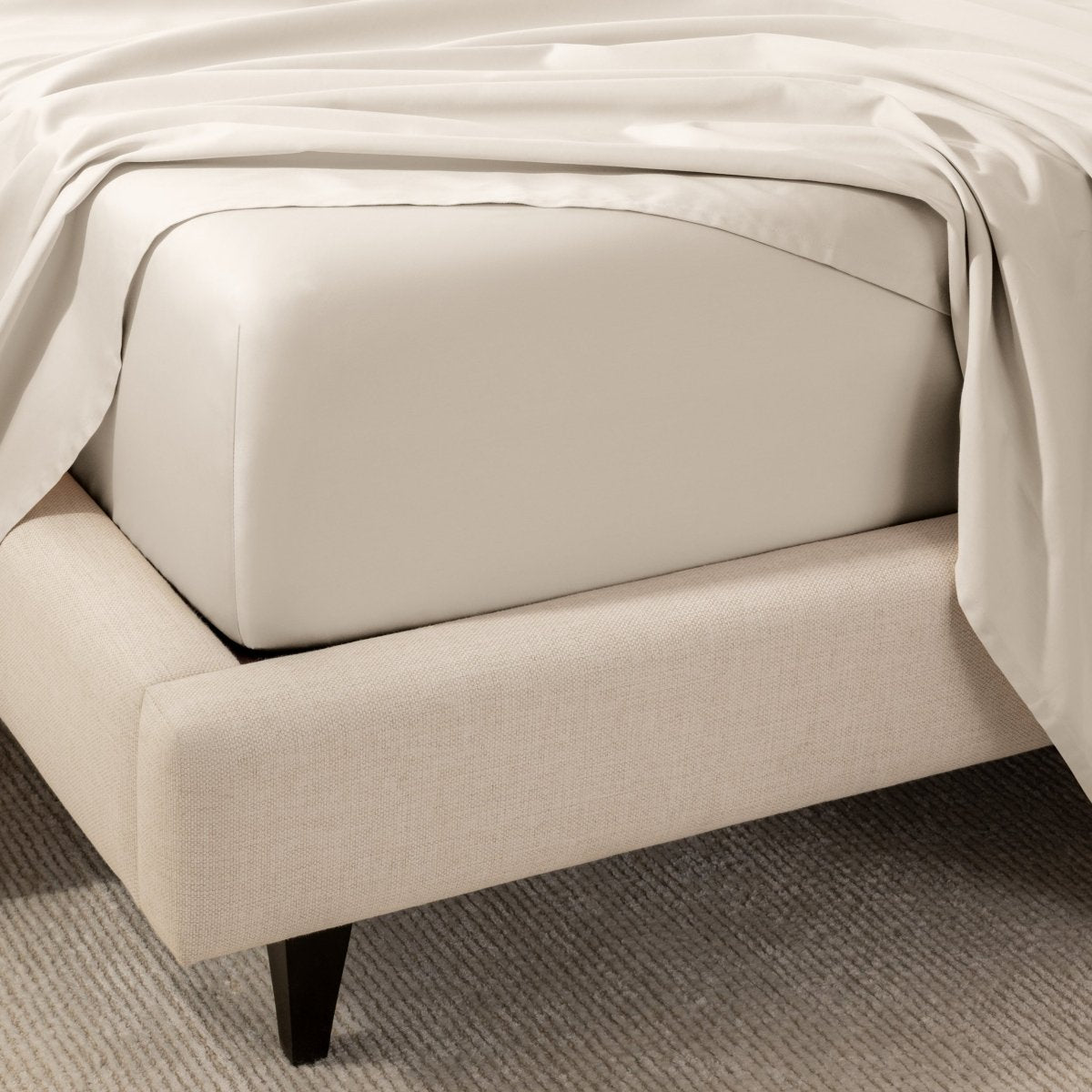 A close-up of the corner of a bed with a fitted sheet and matching flat sheet.