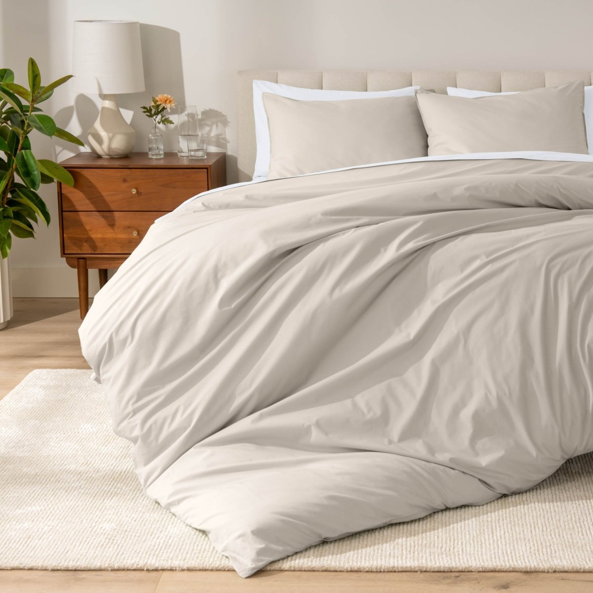 Percale bedding set on a bed in a bedroom with a wooden nightstand and lamp.