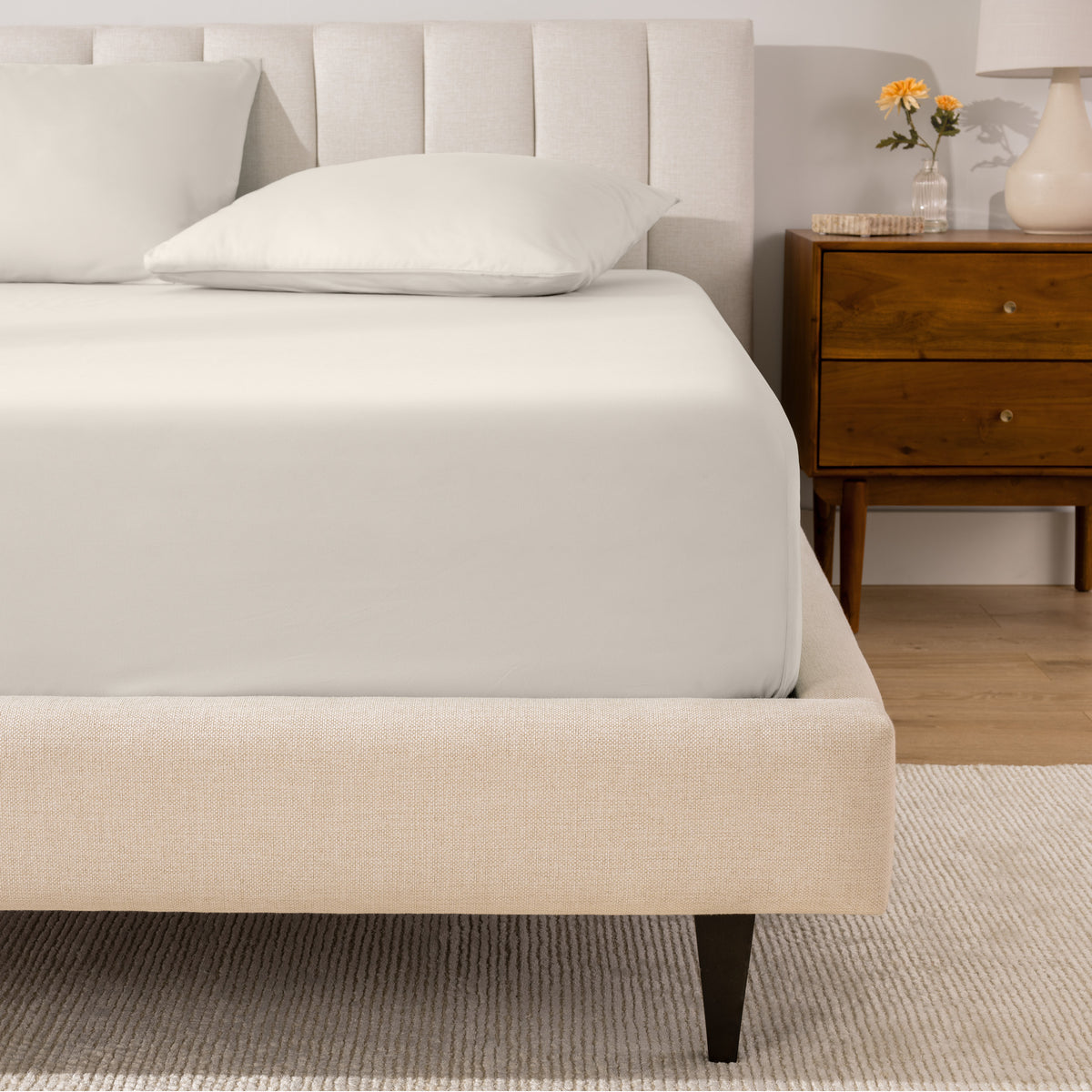 A percale fitted sheet and pillowcases on a bed in a bedroom with a wooden nightstand.