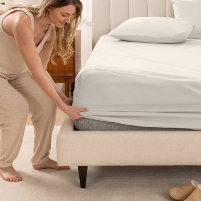 Woman in pajamas adjusting bed sheets on a bed.