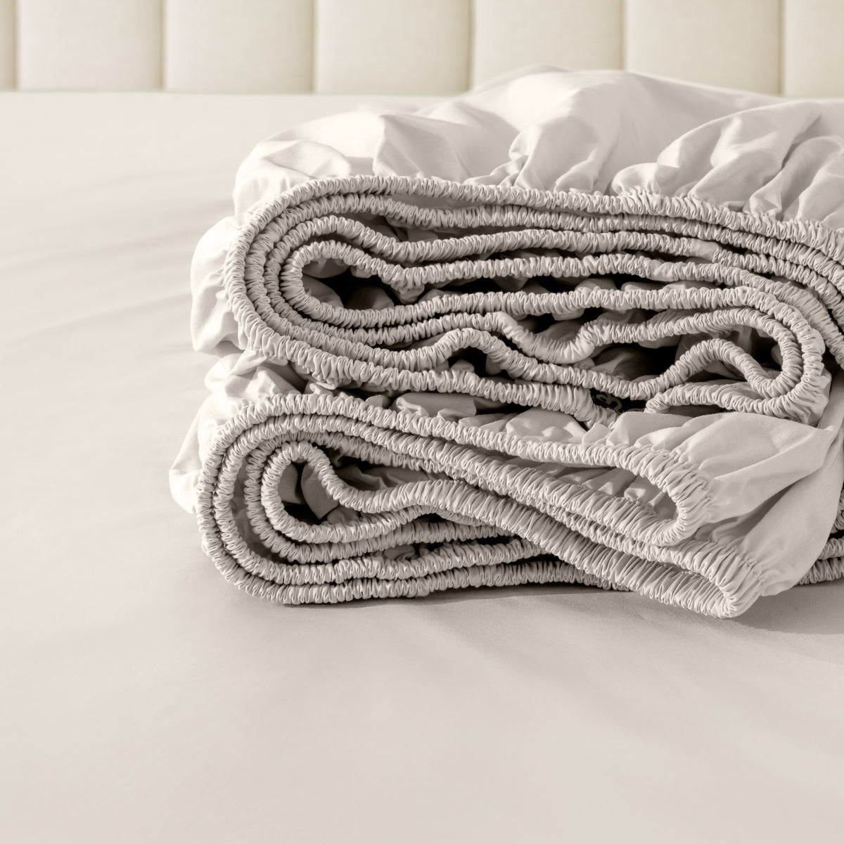 Folded fitted sheet on a bed with a neutral background