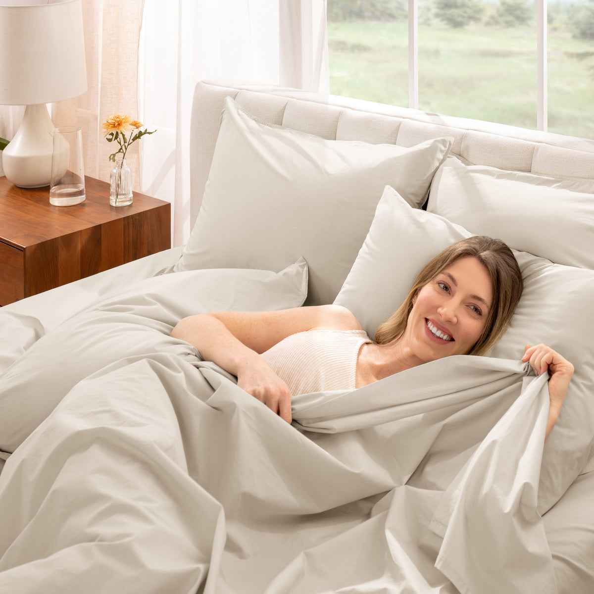 Woman lying in bed with percale bedding in a bright bedroom