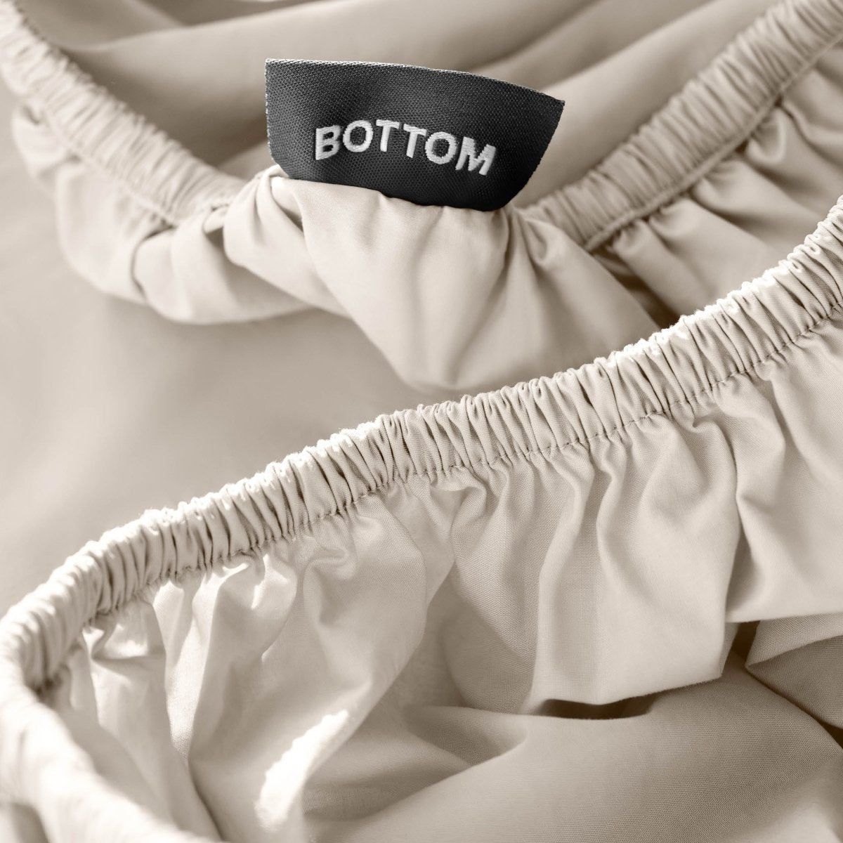 Close-up of a fitted sheet with a black fabric brand label reading BOTTOM.