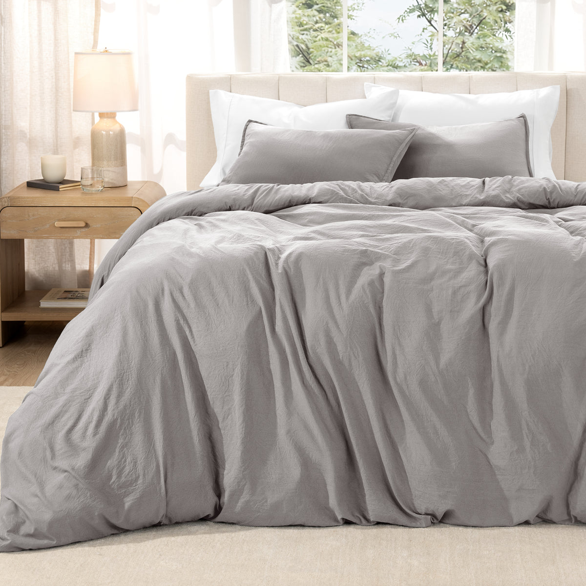 Washed duvet set on a bed in a bright bedroom with a lamp and window.