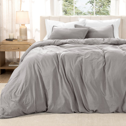 Washed duvet set on a bed in a bright bedroom with a lamp and window.