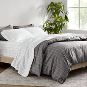 Bed with gray and white grid bedding in a bright room with a plant.