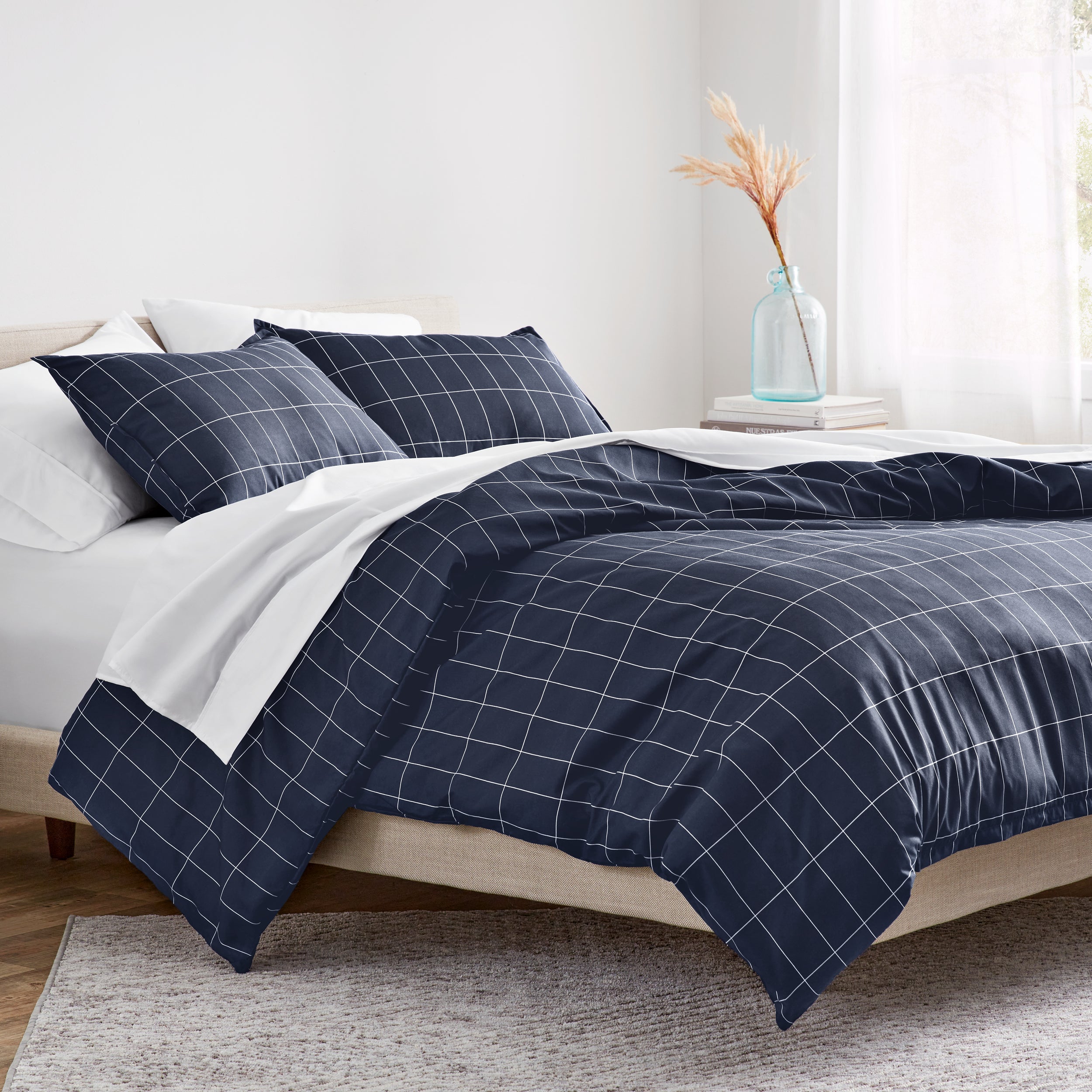 Navy blue grid patterned comforter on a bed in a bright bedroom.