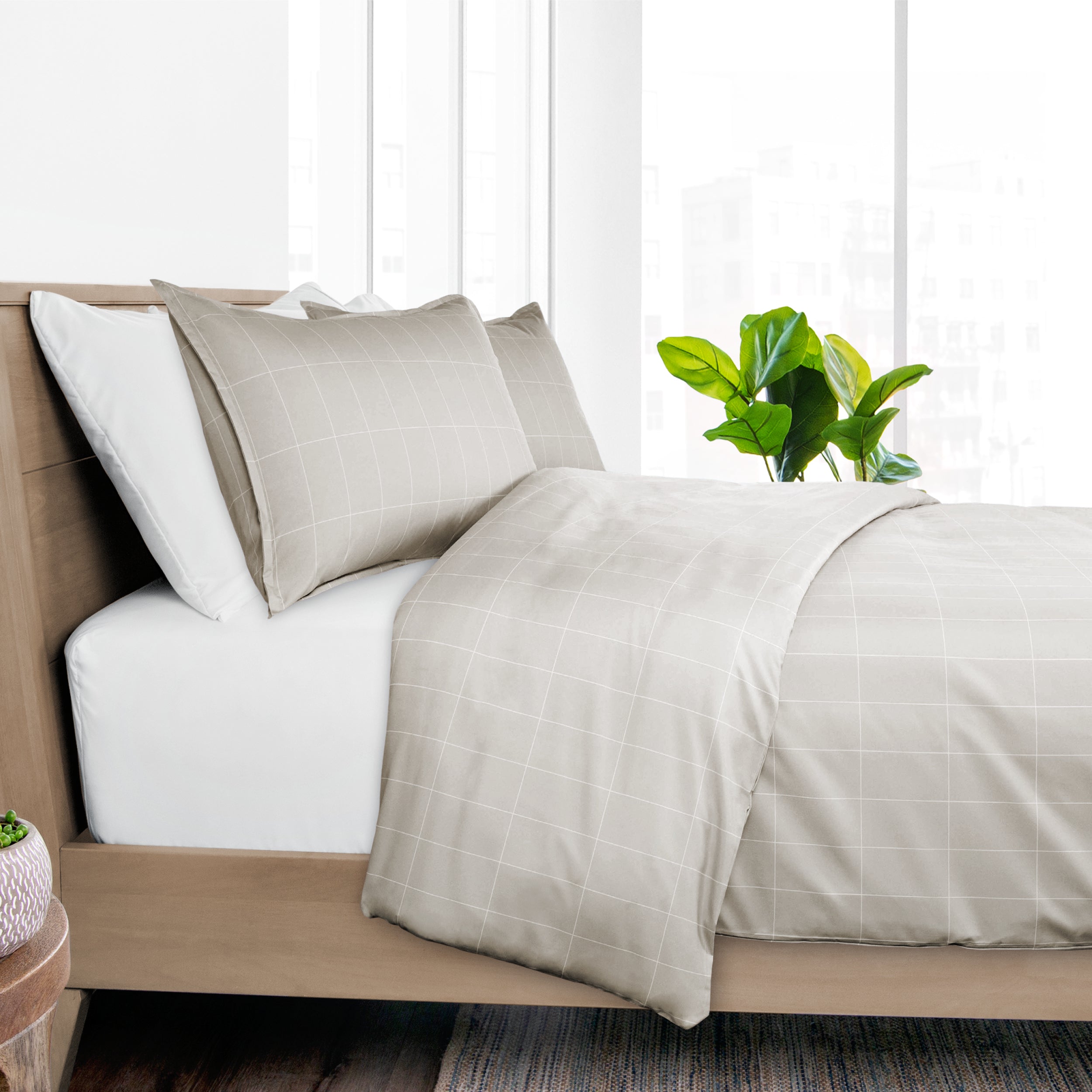 Neatly made bed with beige bedding and pillows, plant on nightstand, wooden headboard.