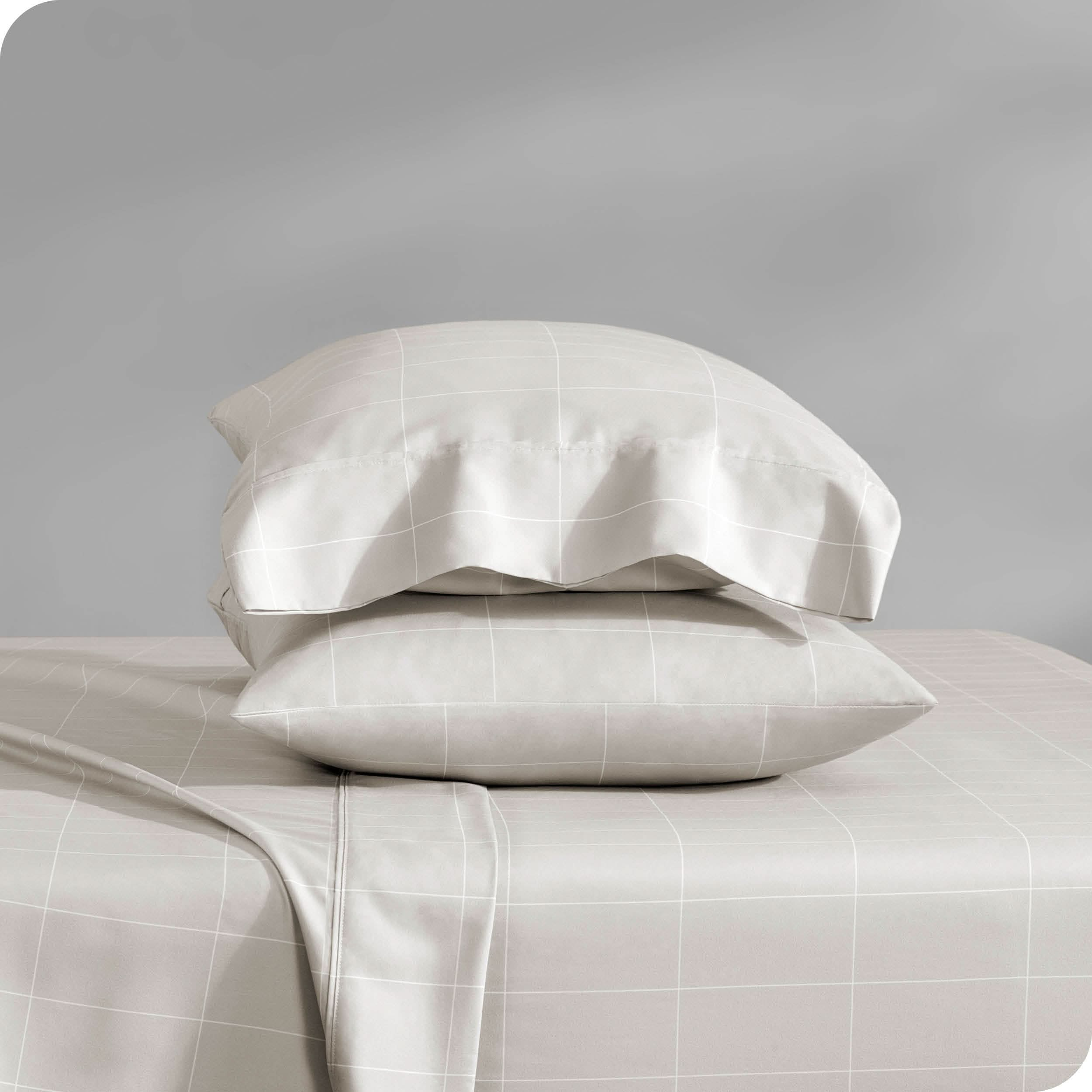 Two pillows with pillowcases on them stacked on a bed