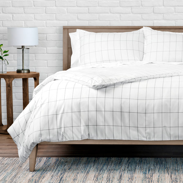 Bed with white grid-patterned bedding against a white brick wall.