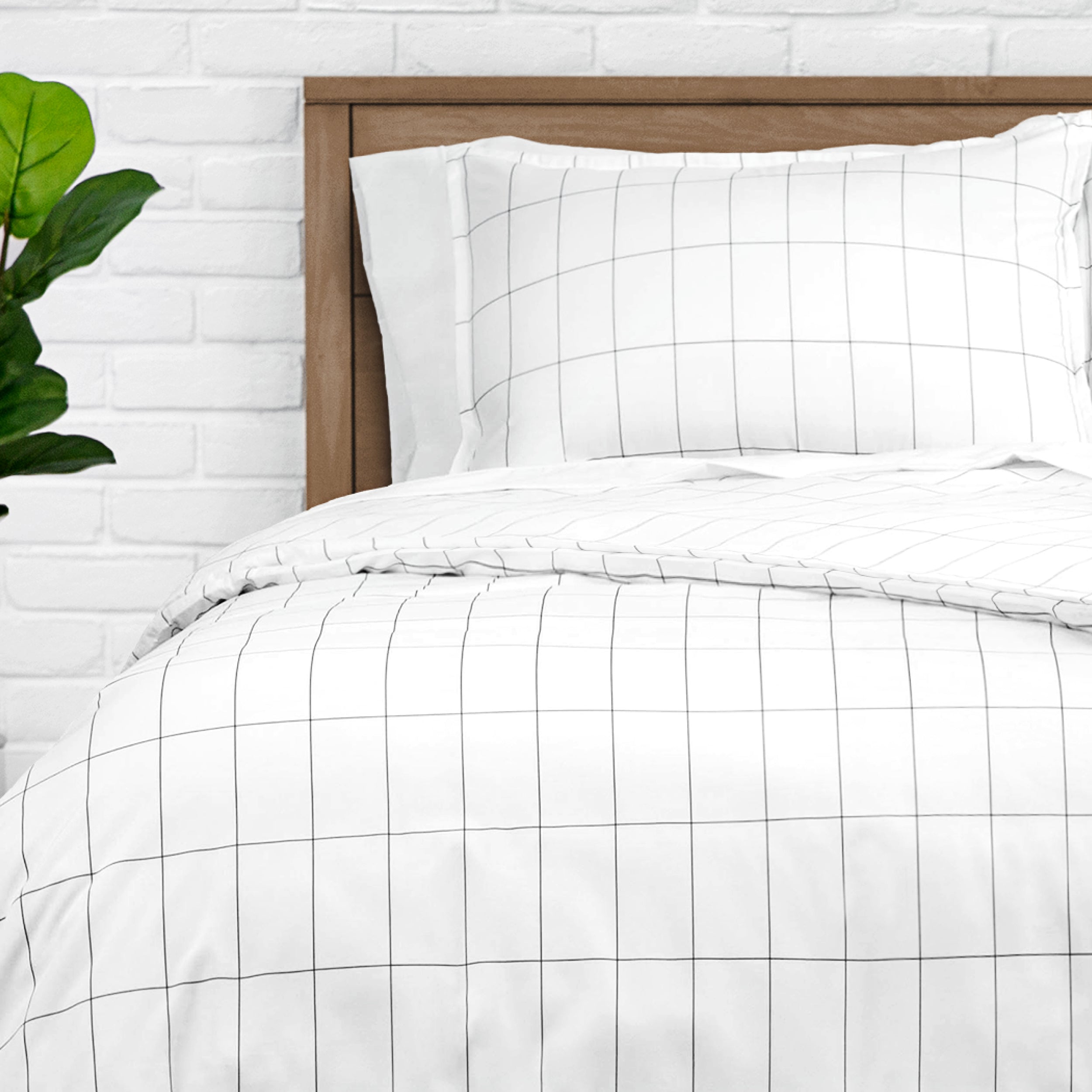 White grid-patterned duvet set on a bed with a wooden headboard, against a white brick wall.