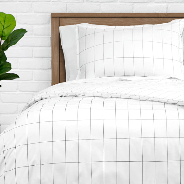 White grid-patterned duvet set on a bed with a wooden headboard, against a white brick wall.
