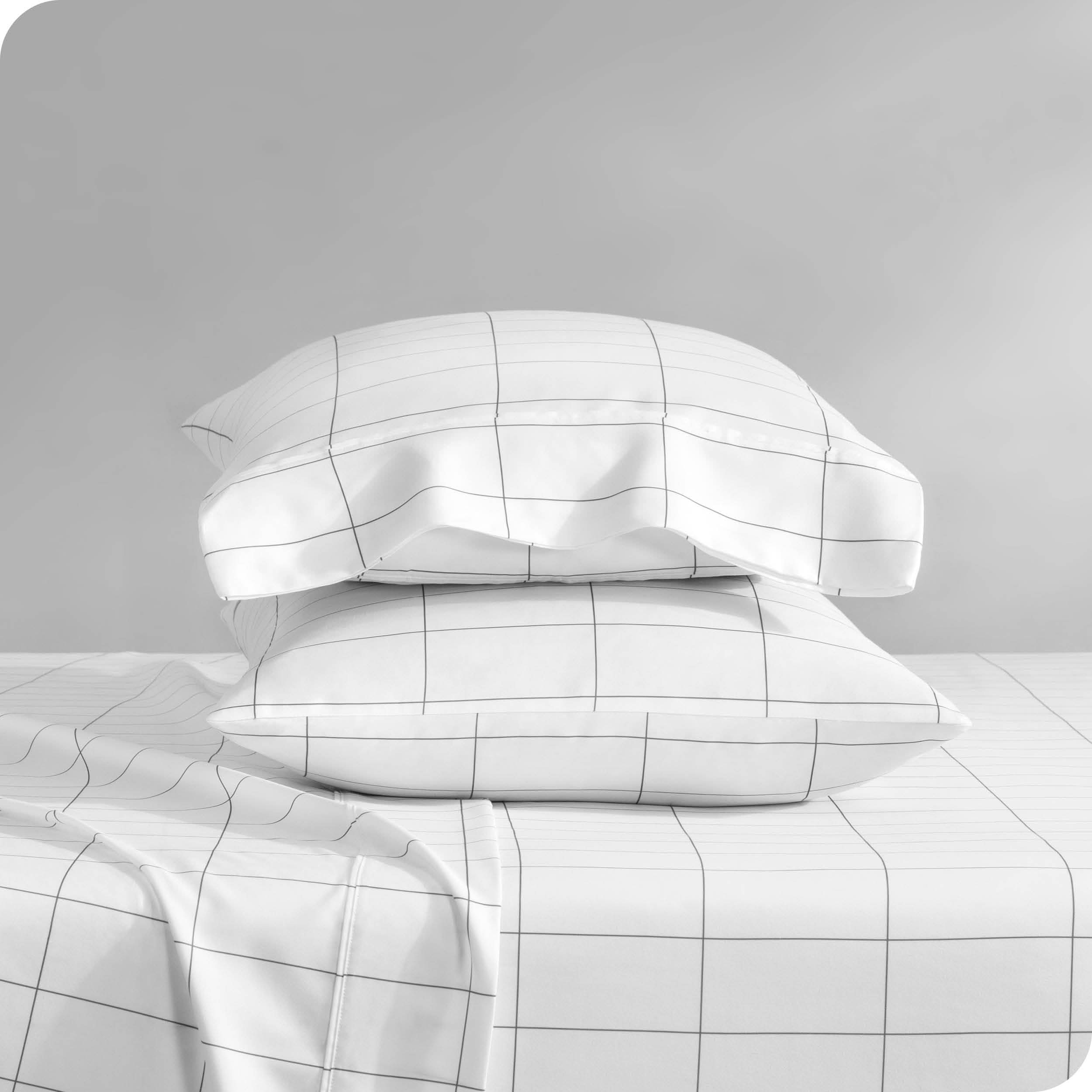 Two pillows with pillowcases on them stacked on a bed