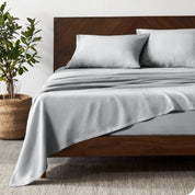 Dark wooden bed frame with grey linen sheets on the mattress
