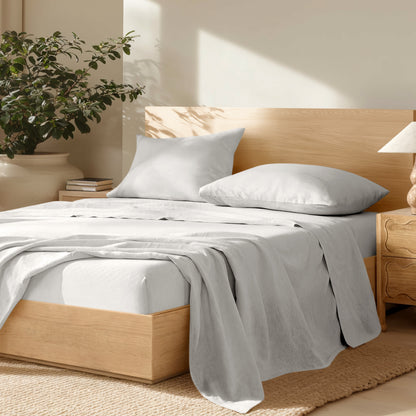 Bedroom with wooden bed frame, linen bedding, and a plant on a nightstand.