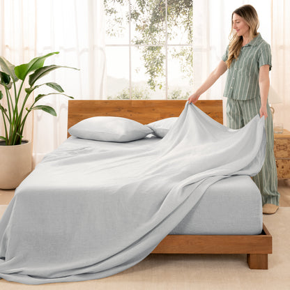 Woman arranging linen sheets on a wooden bed in a bright room with plants.